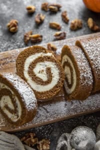 A sliced pumpkin roll dusted with powdered sugar on a cutting board.