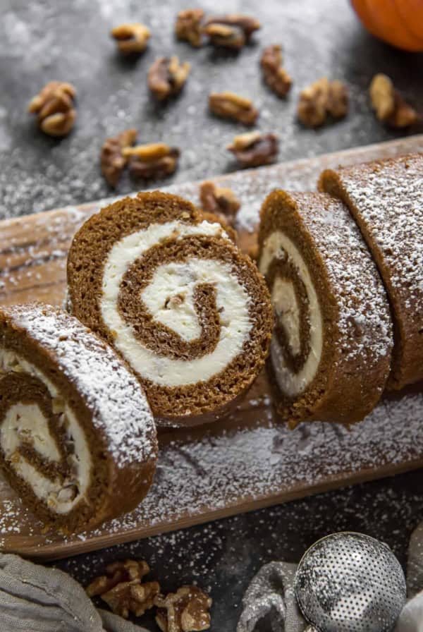 A sliced pumpkin roll dusted with powdered sugar on a cutting board.