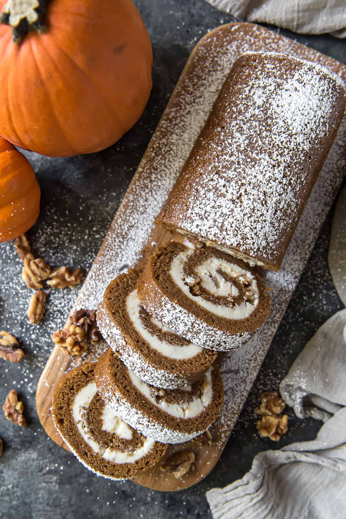 A top down shot of sliced pumpkin roll on a cutting board sprinkled with powdered sugar.