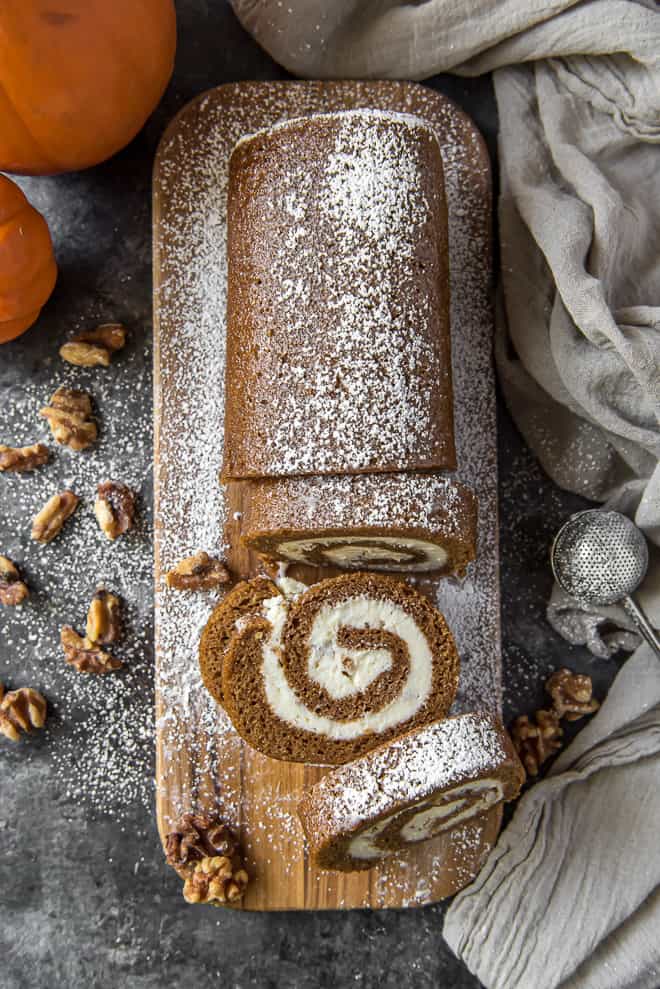 Pumpkin Roll with Cream Cheese Walnut Filling on a wooden cutting board sprinkled with powdered sugar.