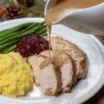 Gravy being poured over slices of turkey on a plate with mashed potatoes.