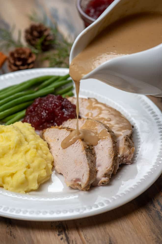 Gravy being poured over slices of turkey on a plate with mashed potatoes.