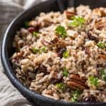 A black bowl filled with wild rice and pecans.