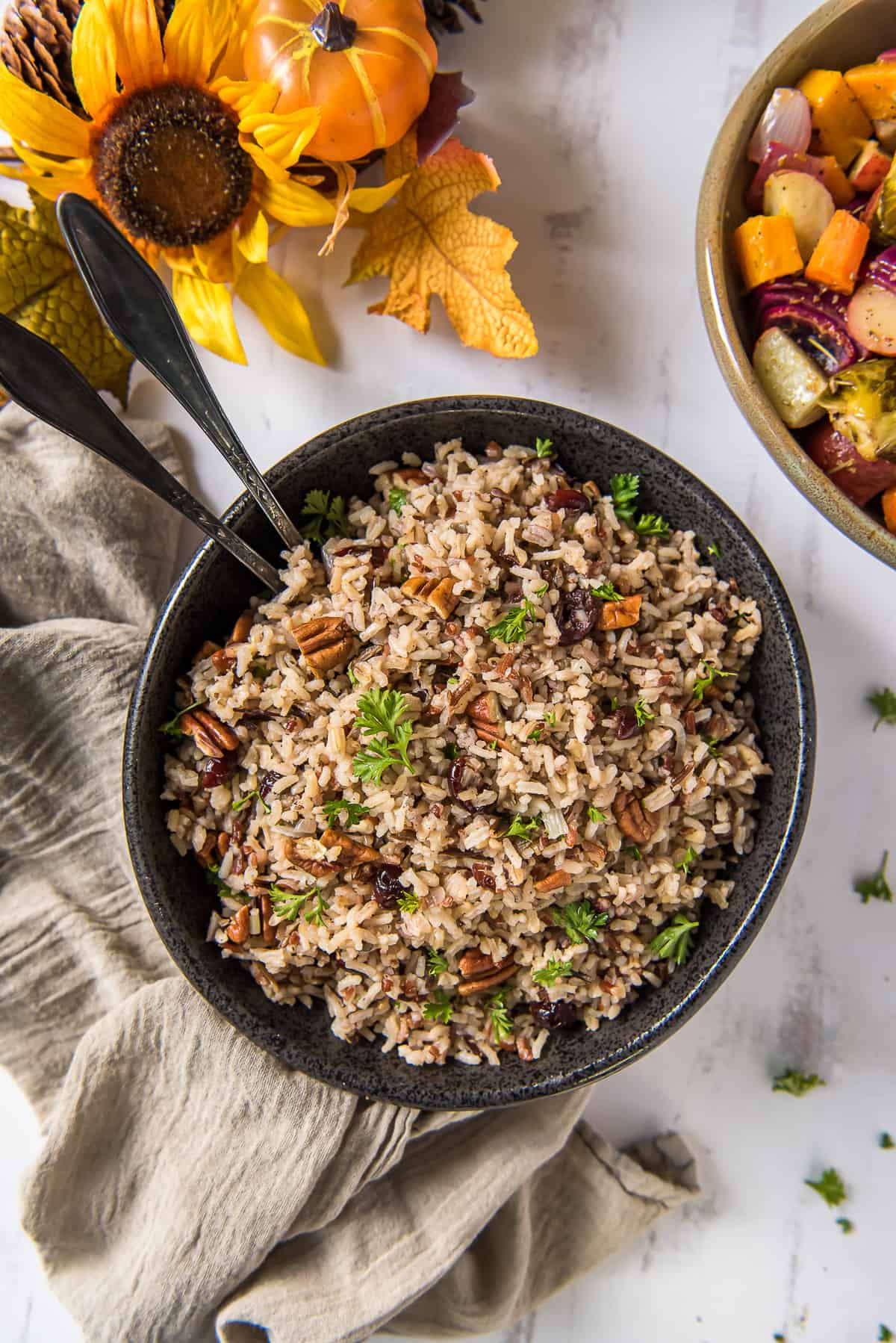 A top down shot of a bowl of wild rice pilaf with serving spoons.