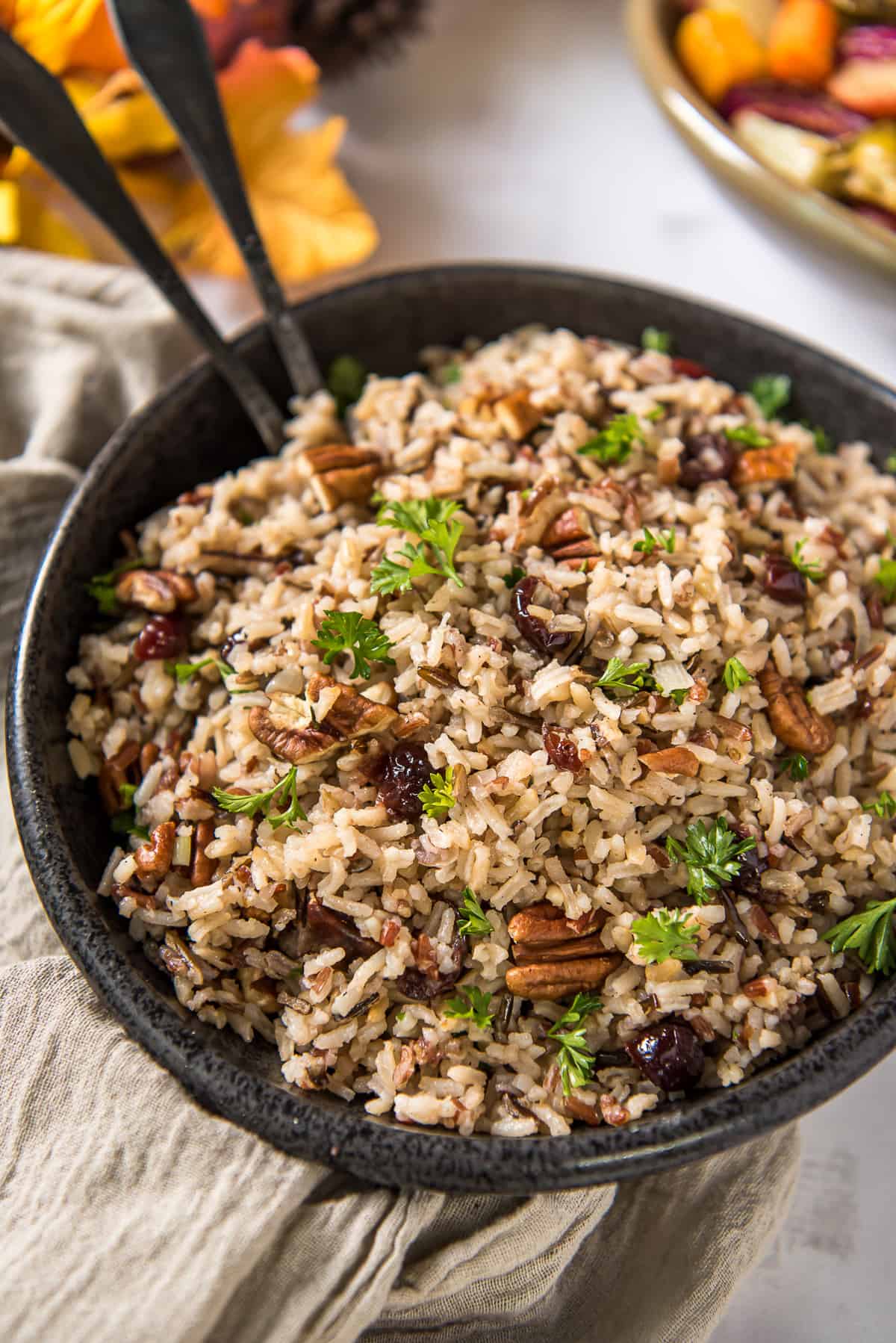 A black serving bowl filled with Wild Rice Pilaf with serving spoons