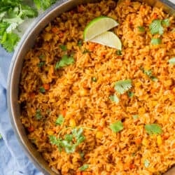 A skillet filled with Mexican rice, cilantro and slices of lime.