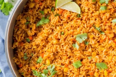 A skillet filled with Mexican rice, cilantro and slices of lime.