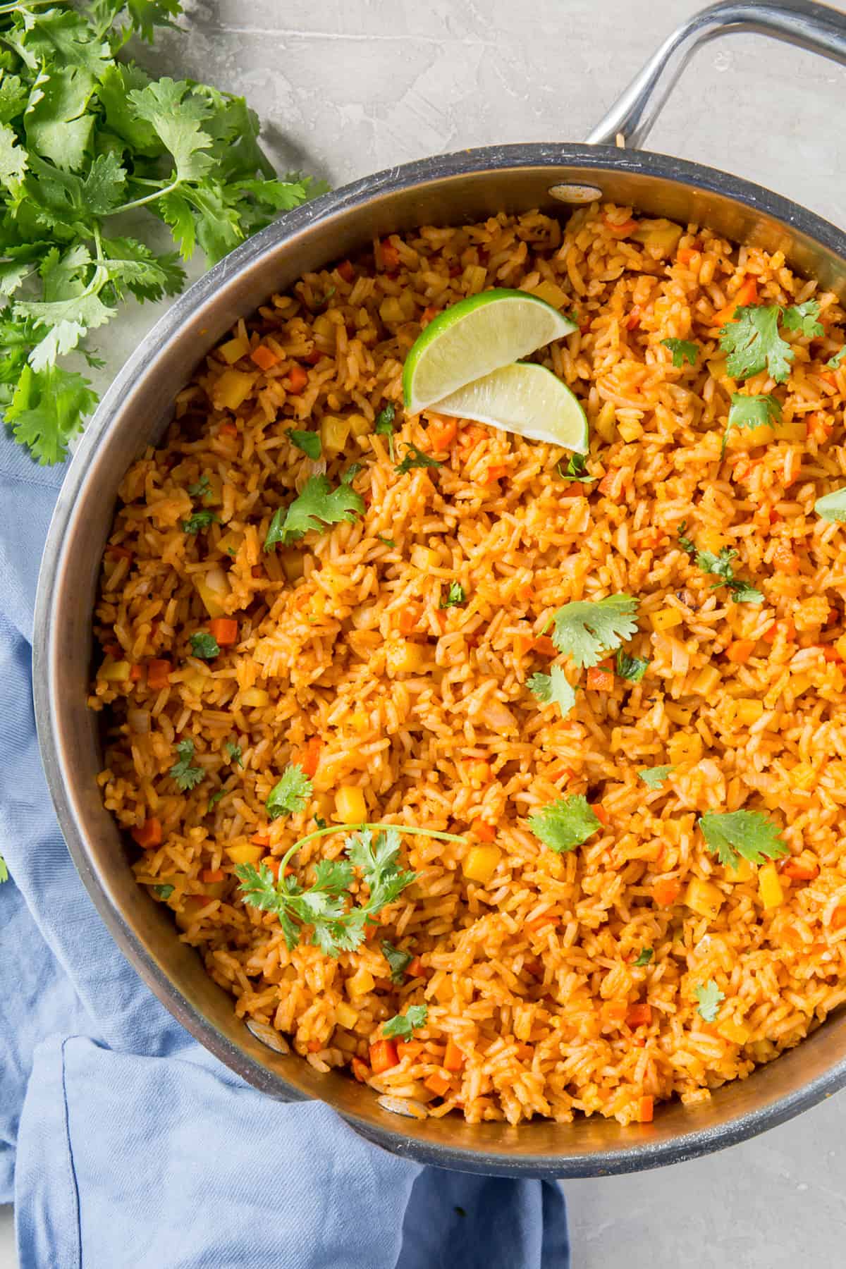 A skillet filled with Mexican rice, cilantro and slices of lime.