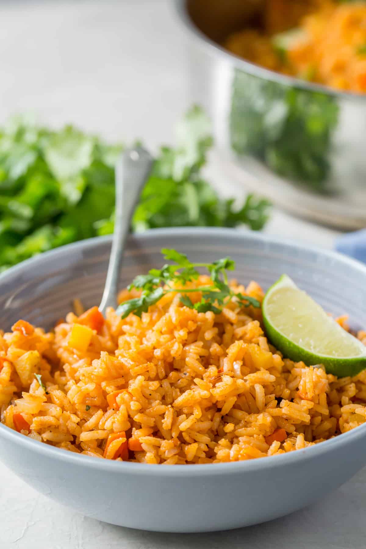 A fork resting in a small bowl of Mexican rice topped with a slice of lime.