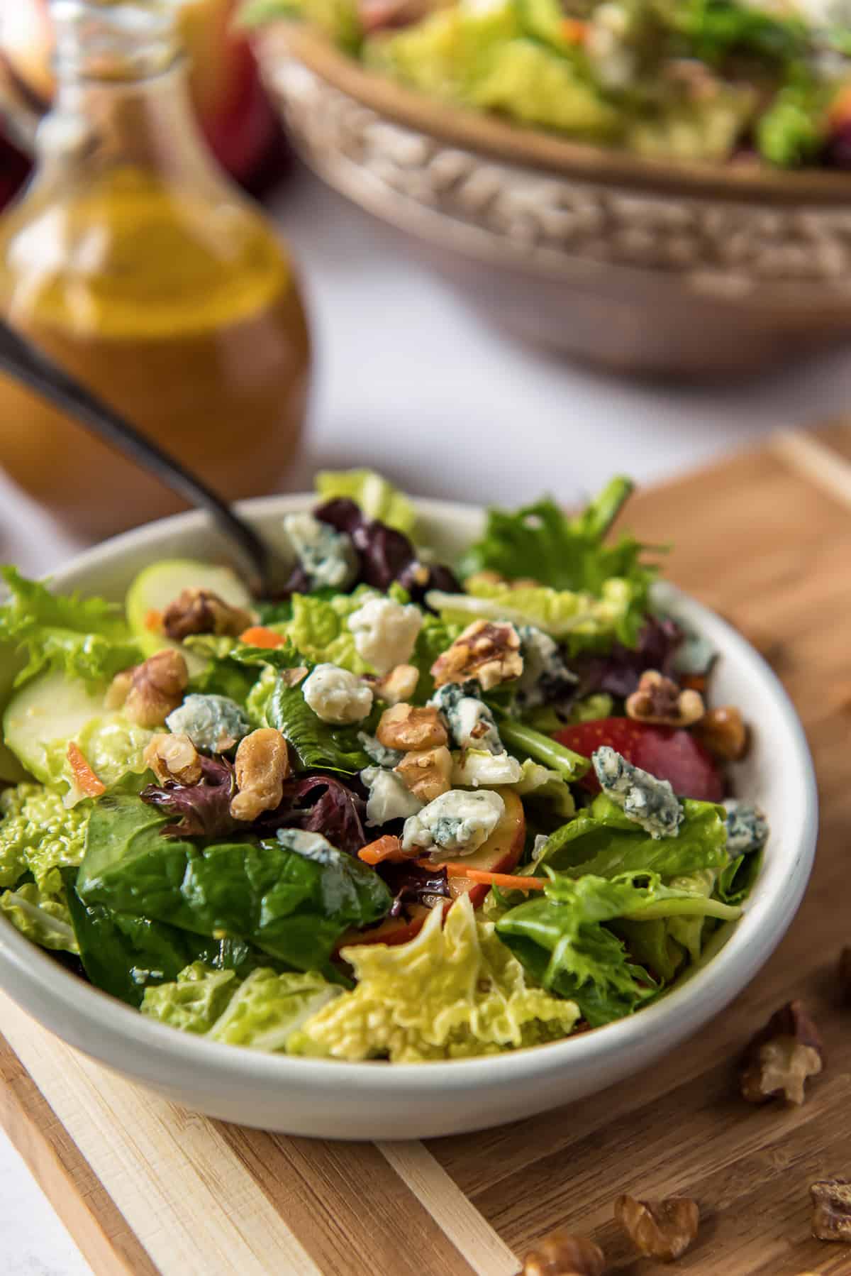 Cabbage Apple Salad in a white serving bowl on a cutting board with salad dressing behind it.