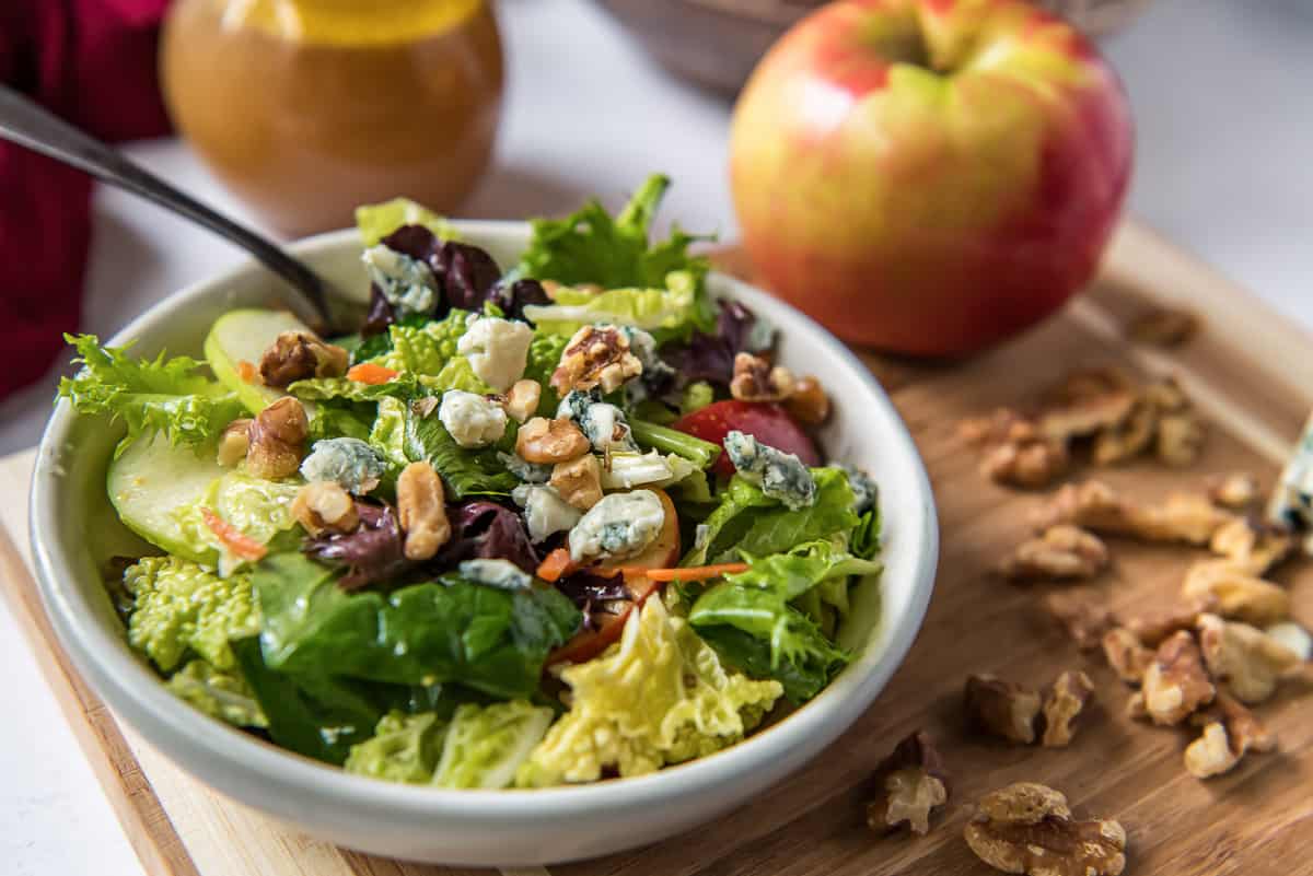 A serving of Apple Cabbage Salad in a white bowl next to apples.