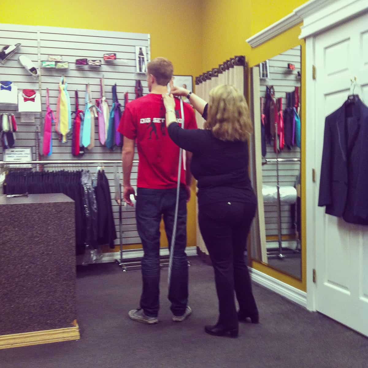 A young man in a red tshirt being measured with a woman with a measuring tape.