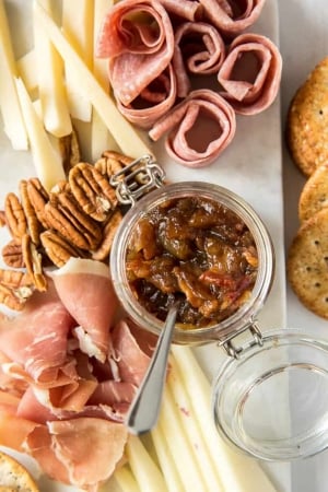 A tray of cheese, meats, nuts, and bacon jam in a small glass container.