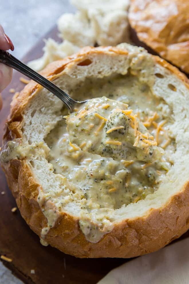 A spoonful of Broccoli Cheese Soup being lifted from the bread bowl.