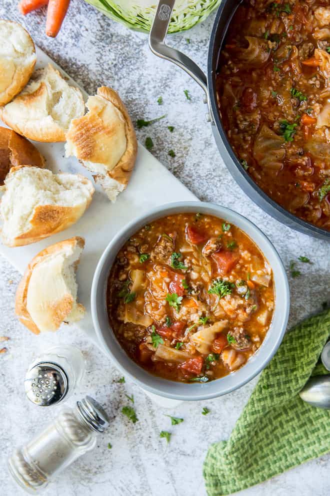 A bowl of soup sits next to the pot with torn pieces of bread around the edges.