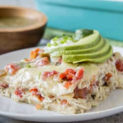 A slice of chicken tortilla casserole topped with slices of avocado on a white plate.