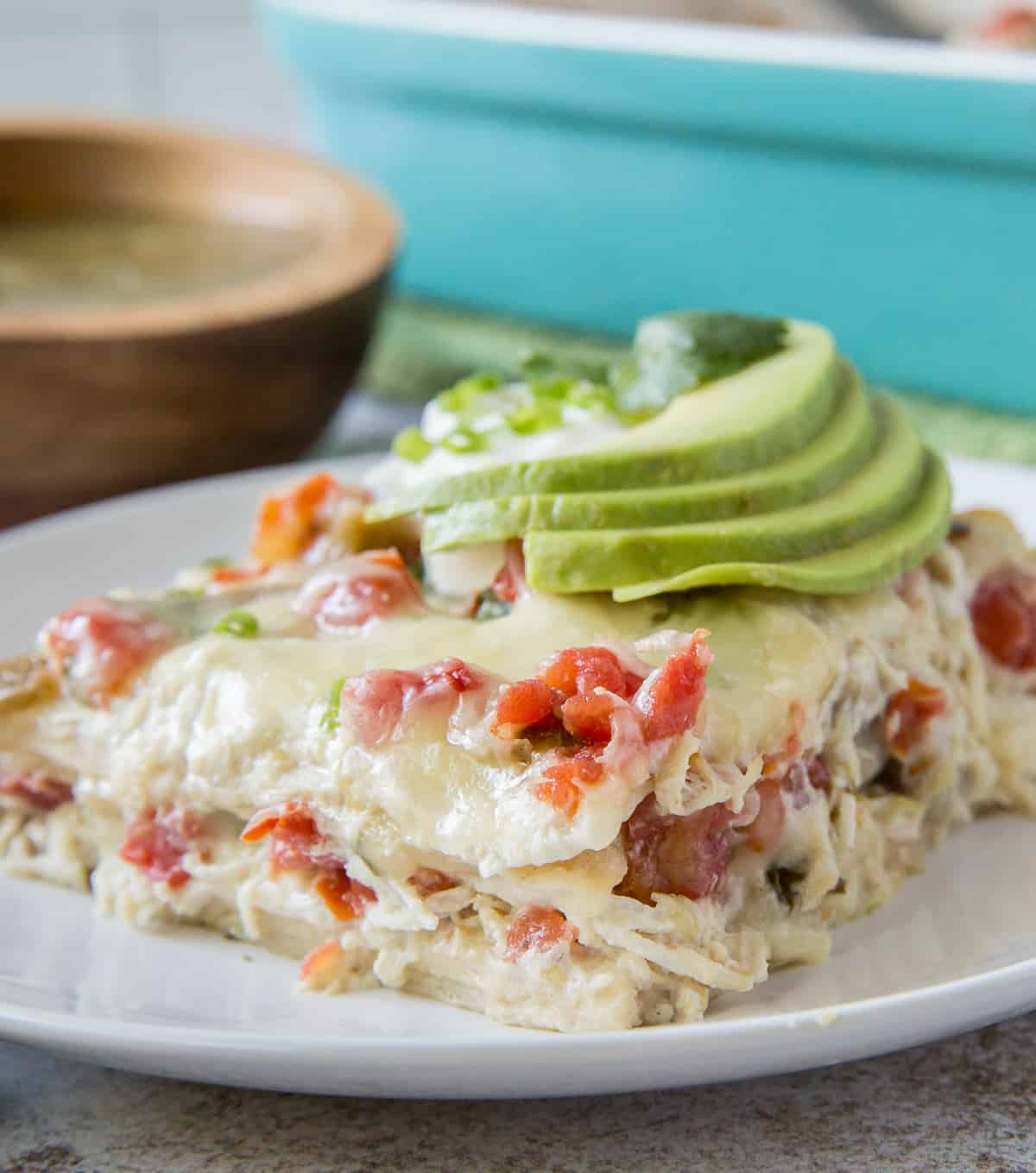 A slice of chicken tortilla casserole topped with slices of avocado on a white plate.