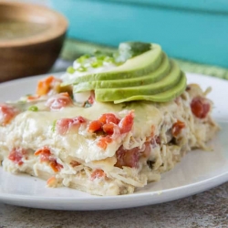 A slice of chicken tortilla casserole topped with slices of avocado on a white plate.