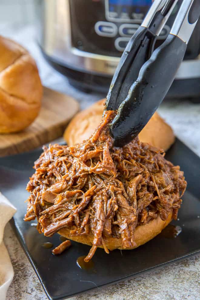 Tongs load up a toasted sandwich bun with shredded Slow Cooker BBQ Beef.