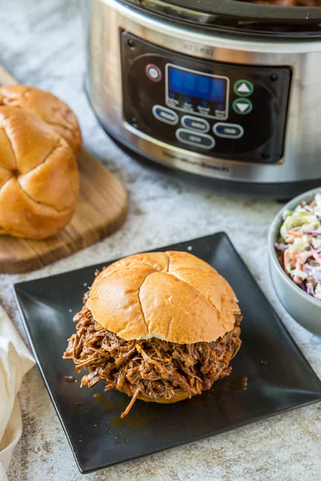 An overhead shot of a Crock-Pot Barbecue Beef Sandwich with a slow cooker in the background.