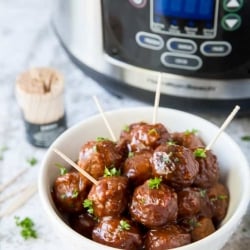 Glazed meatballs in a small white bowl with toothpicks in front of a slow cooker.