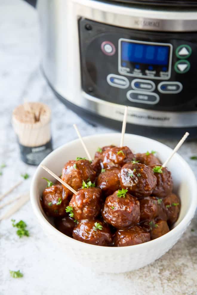 The party meatballs in a small white serving dish with a Crock-Pot in the background.