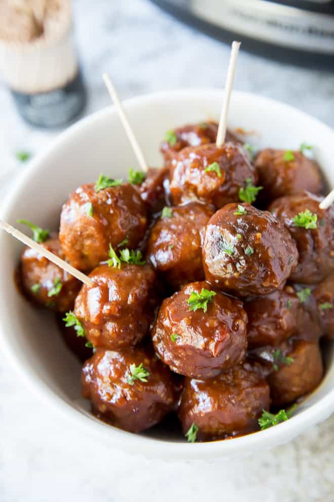 A closeup of a white bowl filled with meatballs with toothpicks sticking out of some of them.