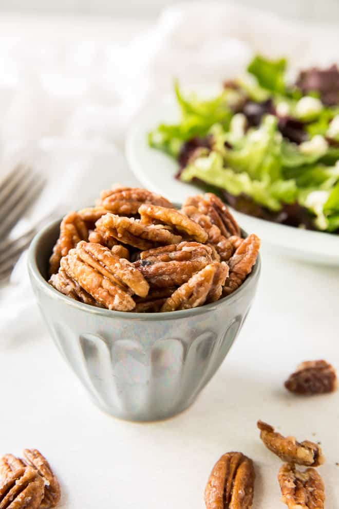 A small bowl full of Glazed Nuts with a salad in the background.
