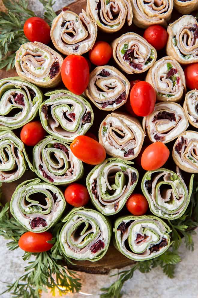 A platter of Holiday Tortilla Pinwheels decorated with grape tomatoes and herbs.
