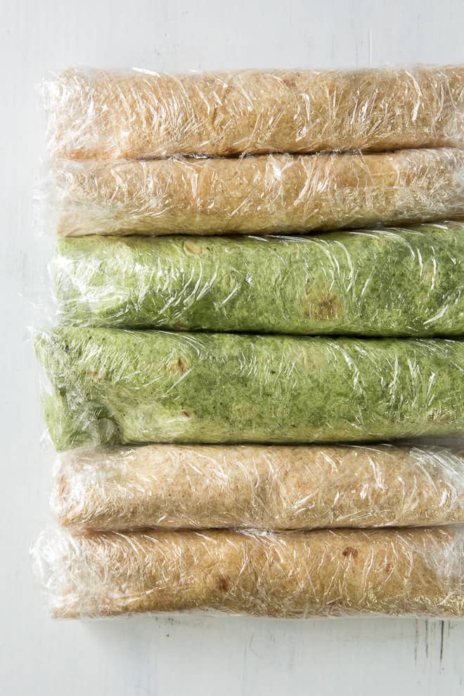 The rolled tortillas tightly wrapped in plastic wrap.