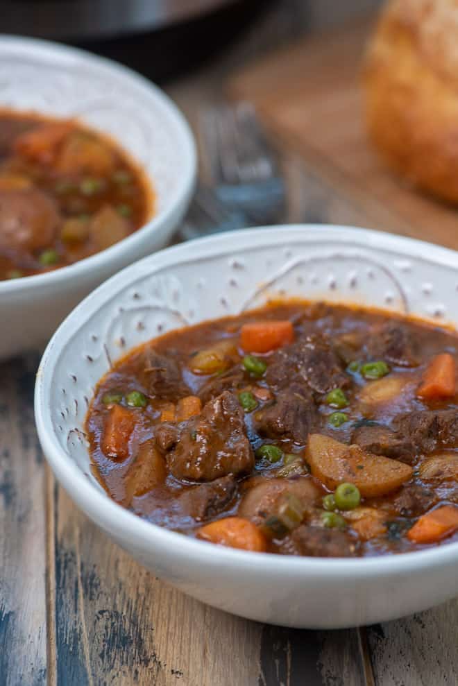 Two bowls of beef stew with bread in the background.