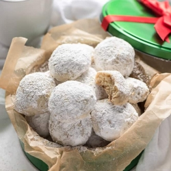 Small round cookies dusted with powdered sugar in a parchment paper lined container.