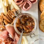 A tray of cheese, meats, nuts, and bacon jam in a small glass container.