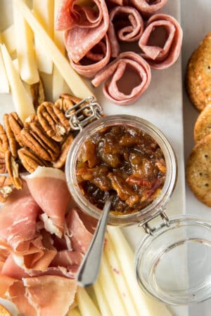 A tray of cheese, meats, nuts, and bacon jam in a small glass container.