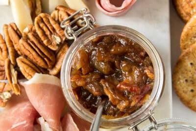 A tray of cheese, meats, nuts, and bacon jam in a small glass container.