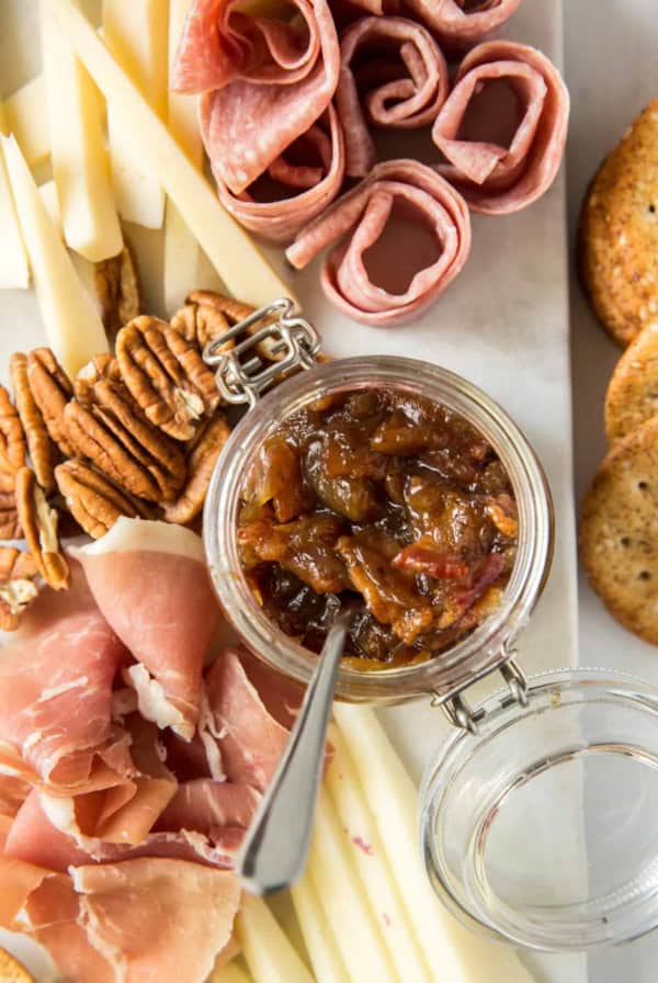 A tray of cheese, meats, nuts, and bacon jam in a small glass container.