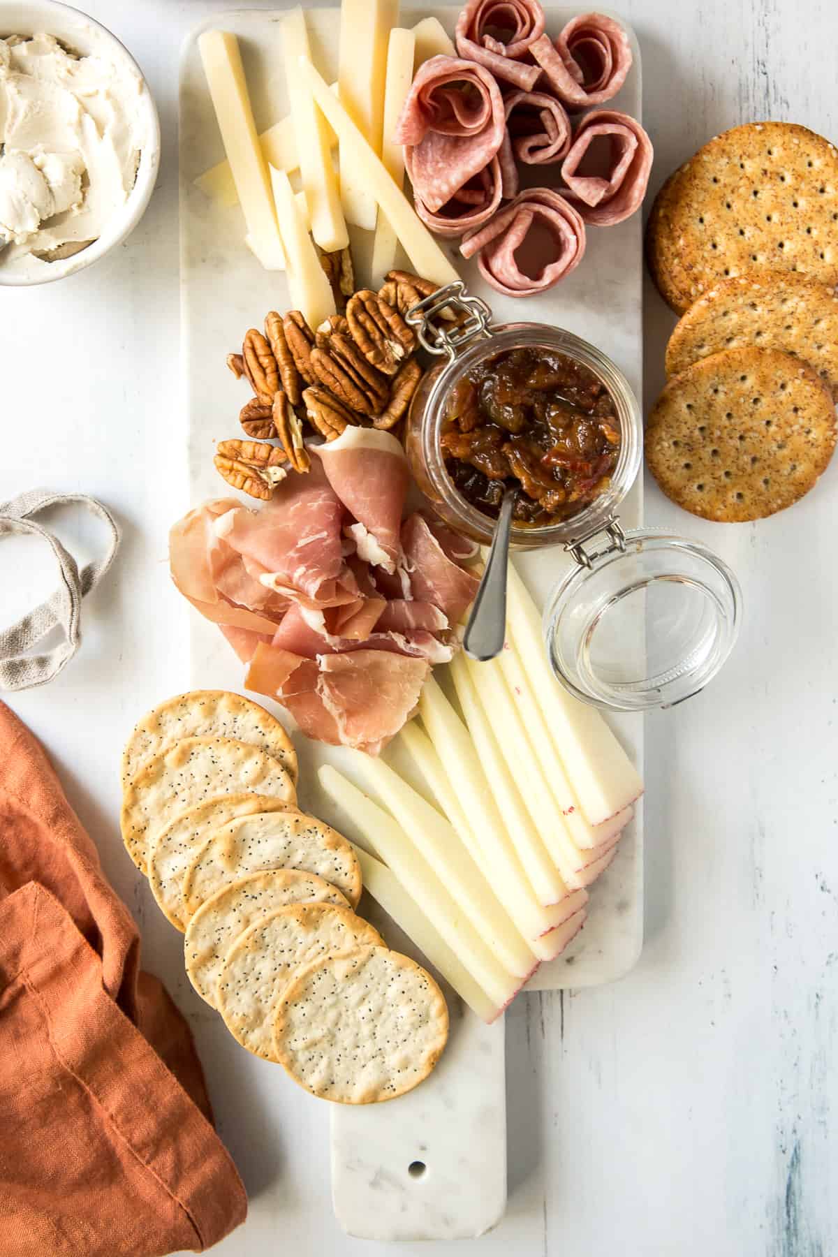 A charcuterie board with cheese, meats, nuts, and bacon jam in a small glass container.