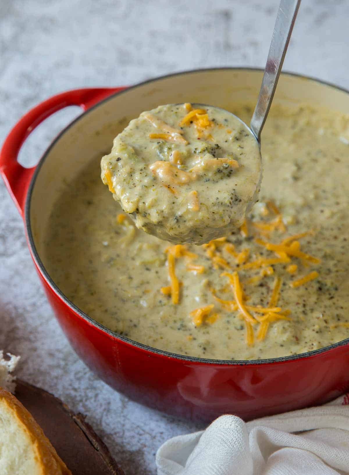A ladle scooping broccoli cheese soup from a red Dutch oven.