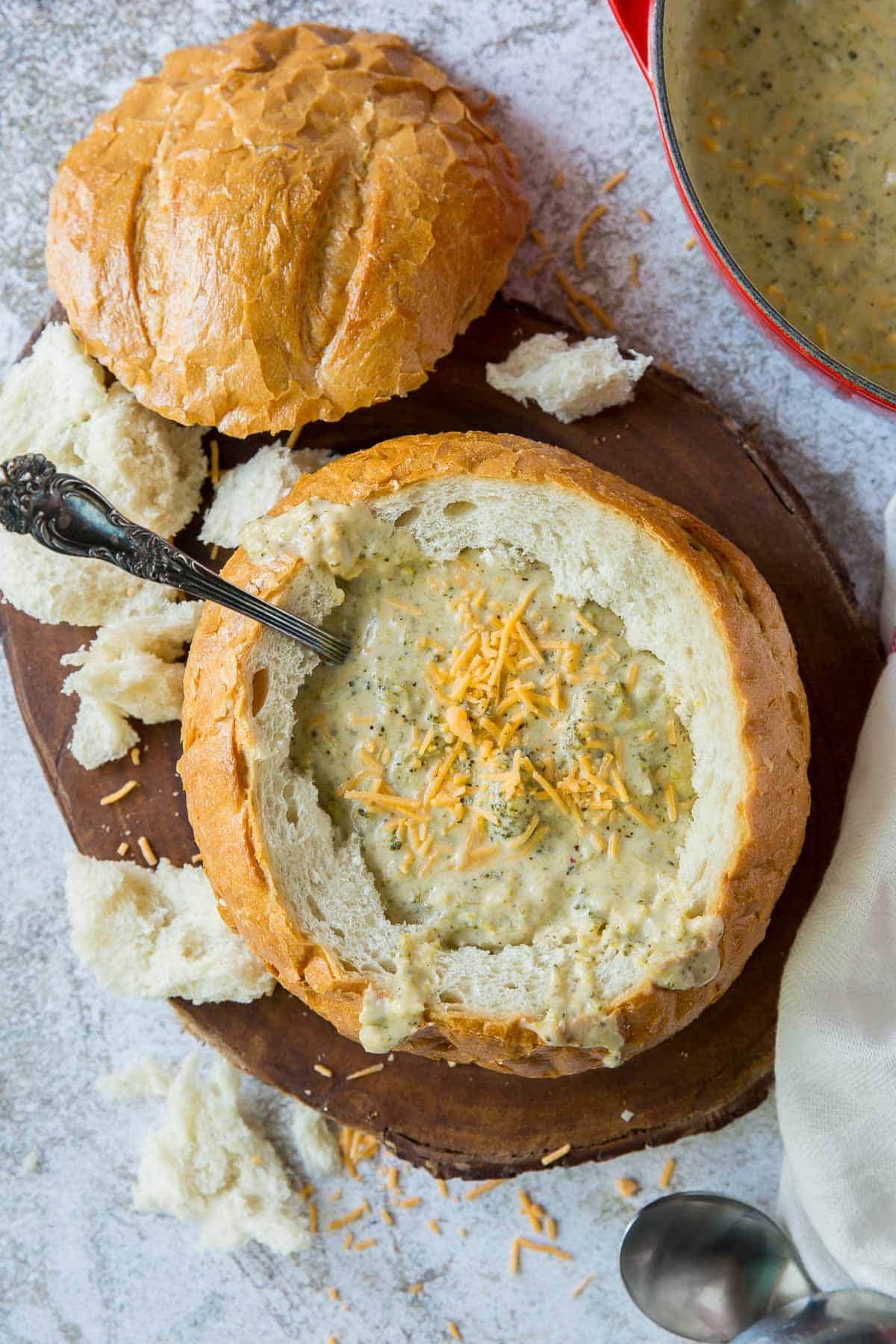 A spoon resting in broccoli cheese soup in a bread bowl.