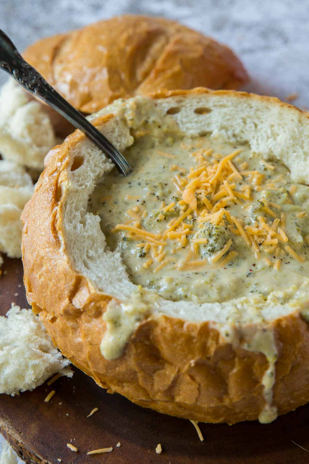 Broccoli Cheese Soup in a round bread bowl topped with shredded cheddar cheese.