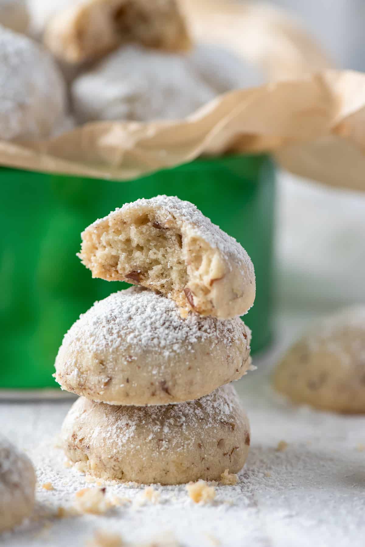 A stack of three powedered sugar dusted Pecan Sandies with a bite missing from the cookie on top.