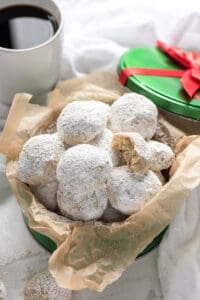 Small round cookies dusted with powdered sugar in a parchment paper lined container.