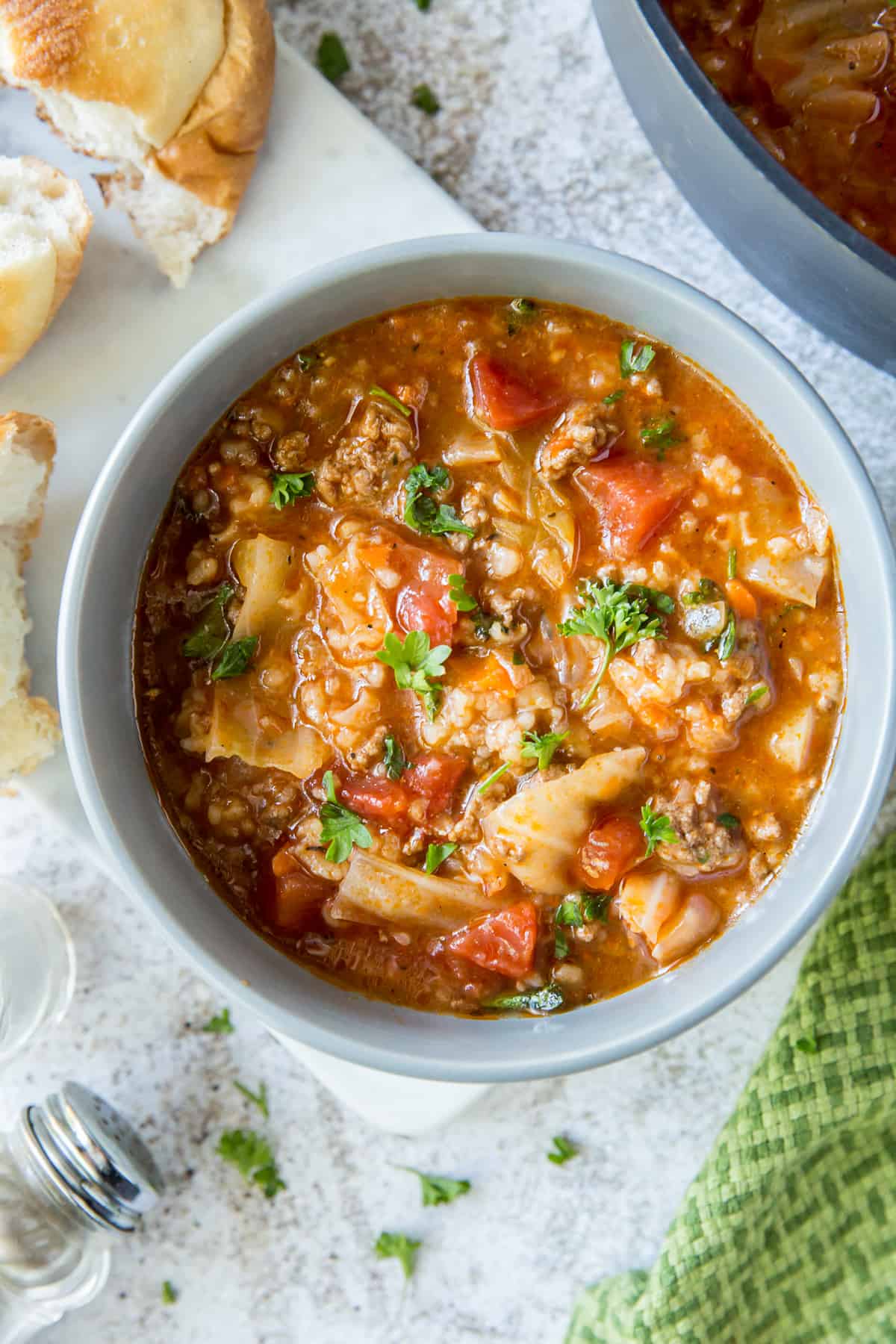 A bowl of Cabbage Roll Soup shot from overhead with pieces of bread around it.