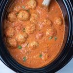 A low cooker insert filled with marinara sauce and meatballs.