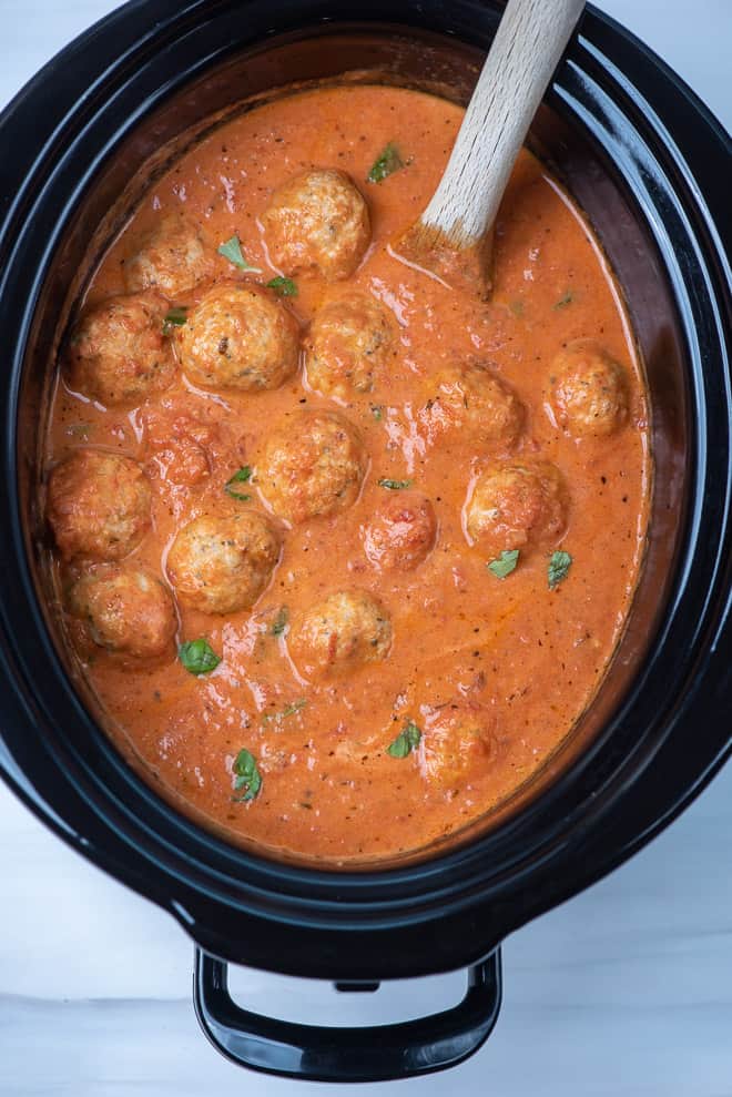 A slow cooker filled with Chicken Parmesan Meatballs in a tomato cream sauce.