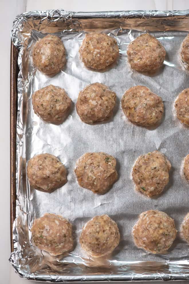 Meatballs made with ground chicken on a foil-lined baking sheet.