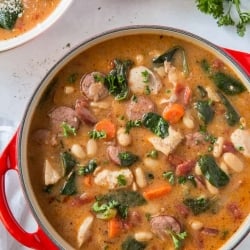 A pot filled with chicken and sausage stew with white beans and spinach.