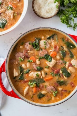 A pot filled with chicken and sausage stew with white beans and spinach.