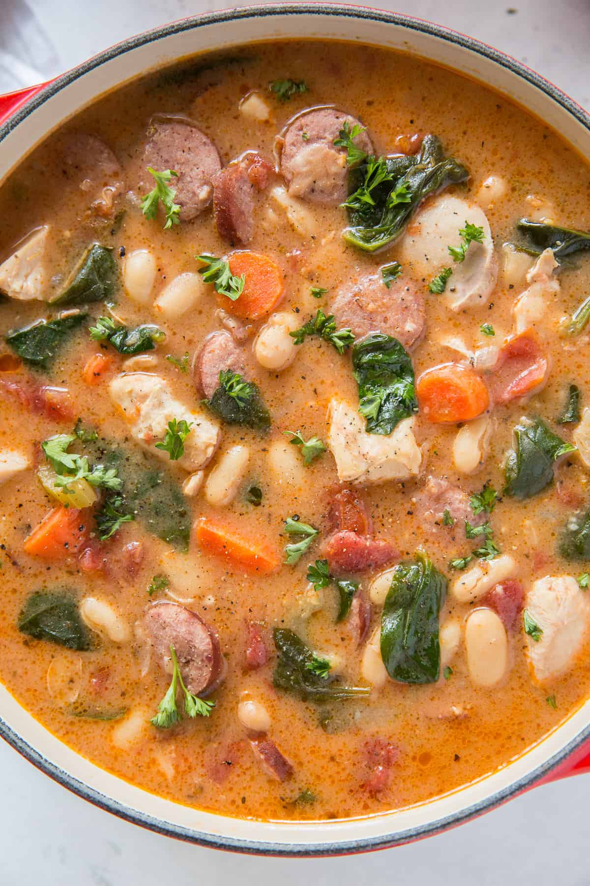 A top down shot of a pot filled with chicken and sausage stew with white beans and spinach.