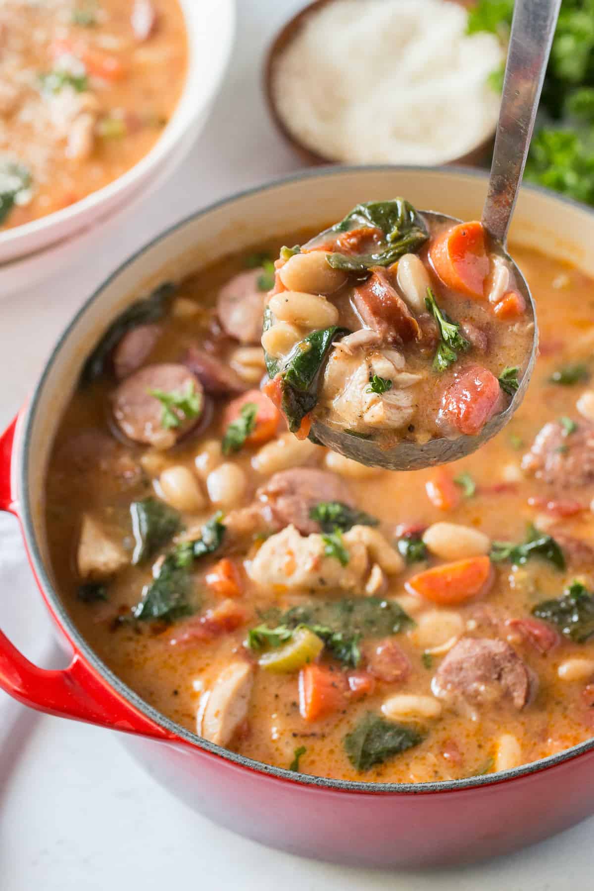 A ladle lifts a scoop of chicken and sausage stew from an orange pot.